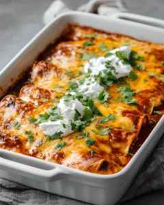 Frozen Burrito Casserole baked with melted cheese, enchilada sauce, sour cream, and fresh cilantro in a white casserole dish.