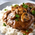 Slow Cooker Salisbury Steak Recipe served over white rice with mushrooms and gravy, garnished with parsley.