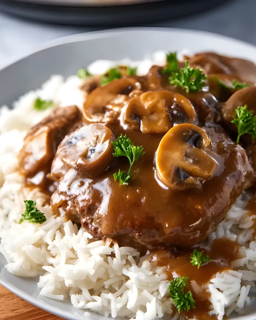 Slow Cooker Salisbury Steak Recipe served over white rice with mushrooms and gravy, garnished with parsley.